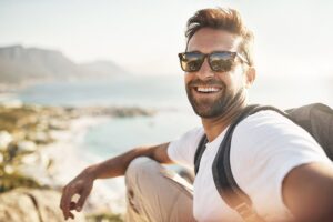a man smiling and taking a photo of himself at the beach after experiencing php benefits on his mental health