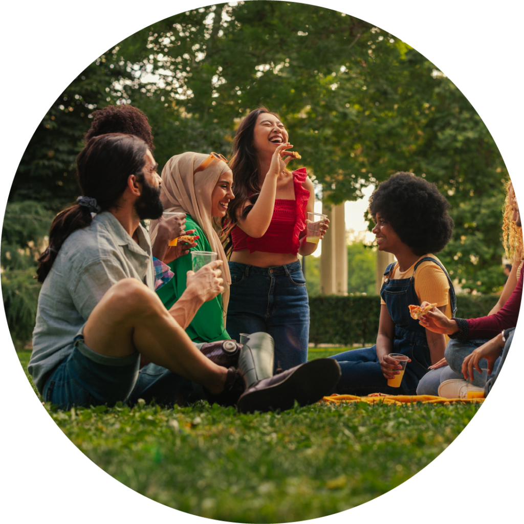 a group of people sit in a park laughing while having a picnic