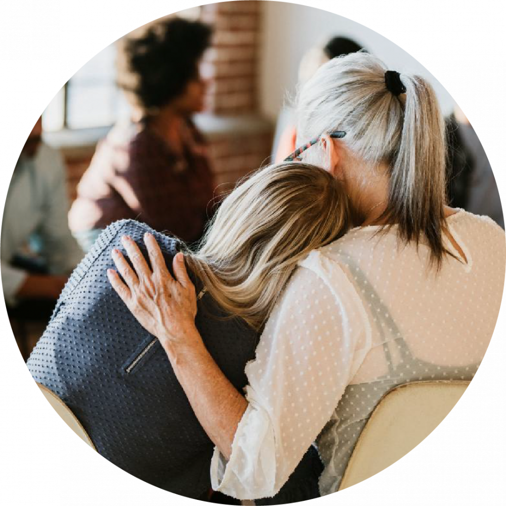 the back view of two women with one woman leaning her head on the other woman's shoulder